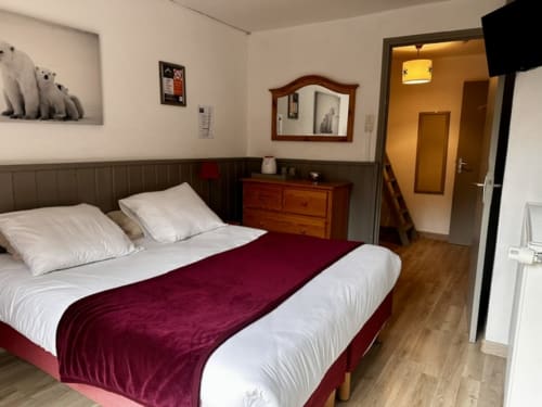 Chambre quadruple supérieure de l'Hôtel la Source avec chemin de table bordeaux, oreillers blancs, commode en bois et accès à la salle de bain privée.
