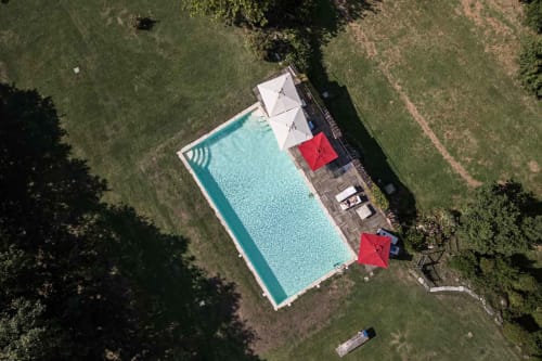 Vista aerea della piscina Donkeys and Roses con ombrelloni bianchi, ombrelli rossi e lettini circondati da verde