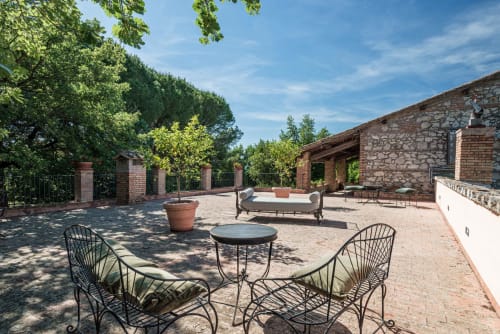 Cortile soleggiato a Donkeys and Roses a Viterbo con sedute in ferro battuto, edifici in mattoni e alberi centenari.