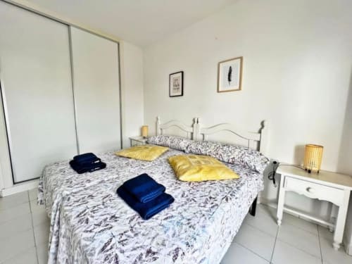 Dormitorio luminoso en apartamento de Fuengirola con ropa de cama estampada, almohadas amarillas y armario espejo