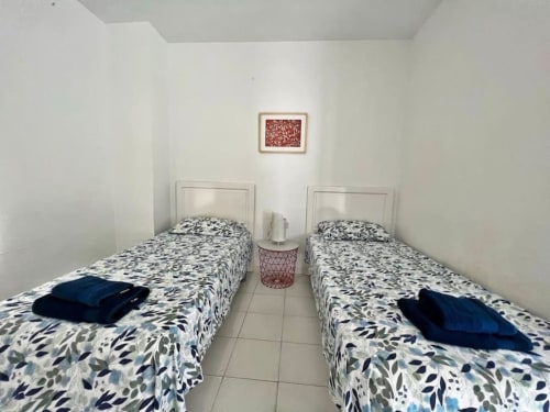 Dormitorio doble en apartamento de Fuengirola con ropa de cama estampada, mesita de noche rosa y cuadros en paredes blancas