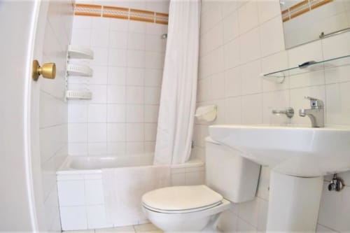 Baño limpio en apartamento de Fuengirola con azulejos blancos, inodoro, lavamanos, ducha y bañera con cortina
