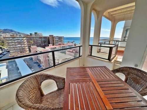 Amplio balcón con vistas al mar en apartamento de Fuengirola, con mesa de comedor de madera, sillas de mimbre y estilo mediterráneo