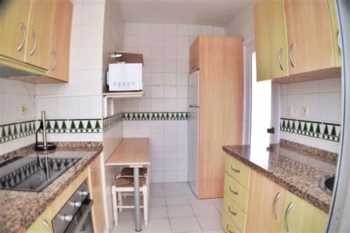 Cocina compacta con armarios de madera, encimeras de granito y electrodomésticos de acero inoxidable en apartamento de Fuengirola