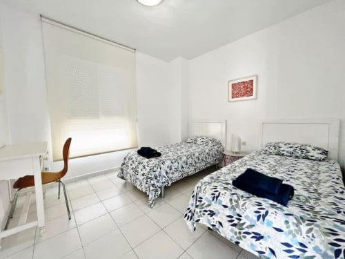 Luminoso dormitorio doble en apartamento de Fuengirola con colchas estampadas, paredes blancas, suelo de baldosas y luz natural