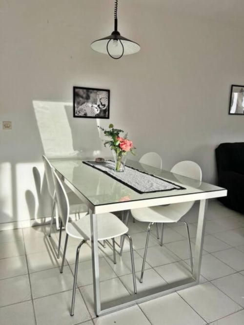 Moderna zona de comedor en apartamento de Fuengirola con mesa blanca, sillas, flores rosas y lámpara colgante