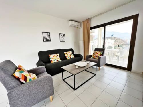 Salón moderno en apartamento de Fuengirola con sofá negro, sillas grises y vistas al mar desde el balcón