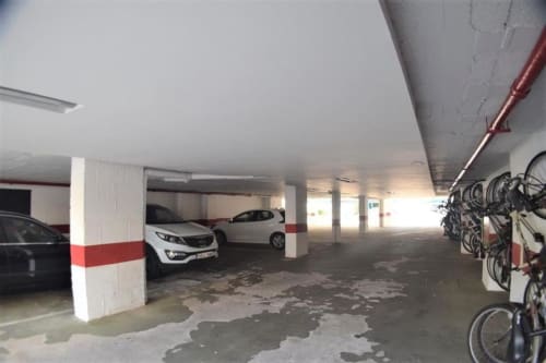 Garaje cubierto de apartamento en Fuengirola con auto blanco, bicicletas, pilares de soporte y tuberías rojas