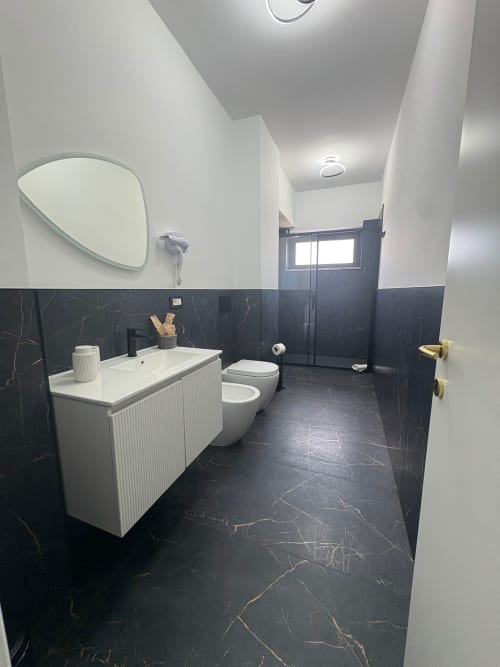 Bagno moderno della Newhouse Hotel Bari con pareti in marmo nero, lavabo bianco, WC, bidet e specchio rotondo