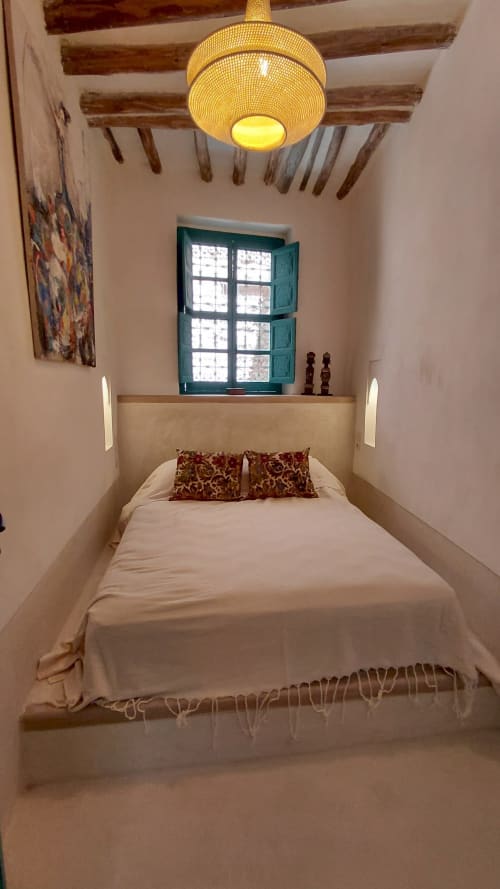 Cozy bedroom at Riad Dar Kleta, Marrakech with bed, brass pendant light, beamed ceiling and turquoise window