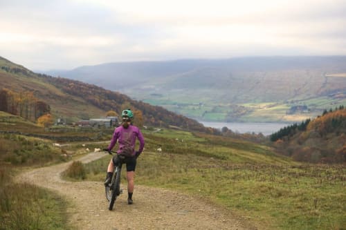 Mountain biker in purple jersey on gravel trail overlooking Scottish valley and loch near Perth