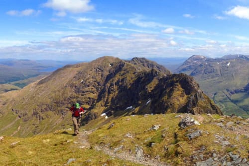 Hiker in red jacket on Scottish mountain trail with dramatic peaks and valley views near Perth