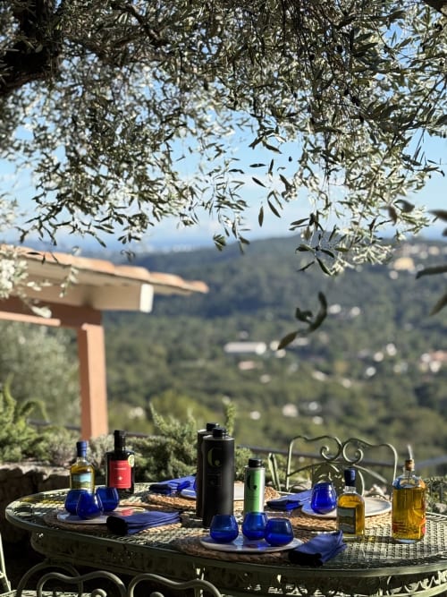 Outdoor terrace at Pipa Polaris with olive branches, blue glassware, and valley views in Spéracèdes, France