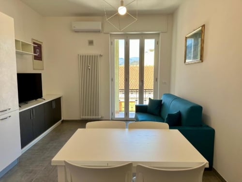 Soggiorno moderno con tavolo da pranzo, divano blu, cucina e balcone con vista su Finale Ligure