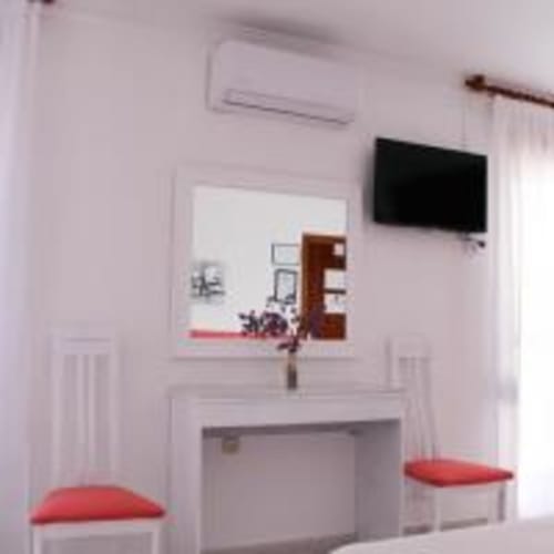 Habitación triple de Hostal las Dunas con TV, aire acondicionado y cojines rojos en Cabo de Gata, Almería