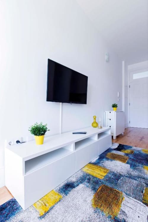 Sala de estar moderna em Bom Porto com TV na parede, móveis brancos, detalhes em amarelo e tapete estampado