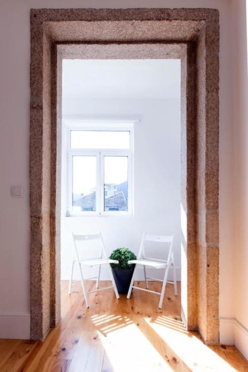 Quarto moderno e luminoso no Bom Porto Apartments com cadeiras brancas, planta em vaso e grandes janelas com vista para a paisagem urbana do Porto