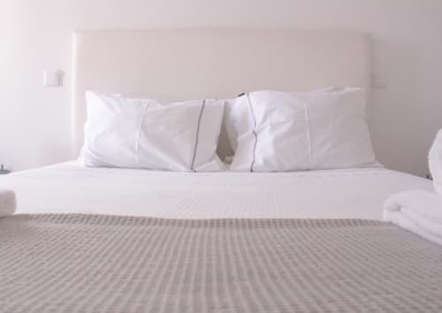 Quarto limpo no Bom Porto Apartments com almofadas brancas, colcha cinza e cabeceira rosa pálido no Porto
