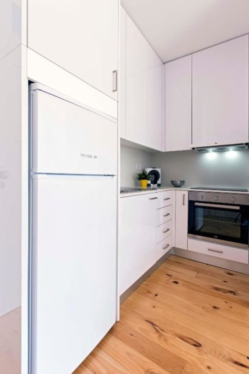 Cozinha moderna no apartamento Bom Porto com armários rosa, geladeira branca, forno embutido e piso em madeira no Porto.