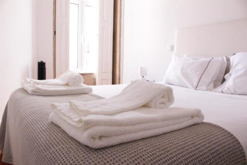 Quarto do Bom Porto Apartments com toalhas brancas dobradas na cama, travesseiros brancos e vista da cidade do Porto