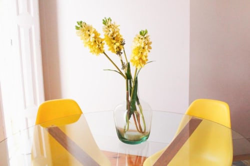 Cadeiras de jantar amarelas em mesa de vidro com flores amarelas frescas em vaso no Bom Porto Apartments, Porto