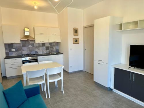 Cucina moderna e zona living dell'appartamento Welcome Holiday a Finale Ligure con tavolo da pranzo e mobili bianchi