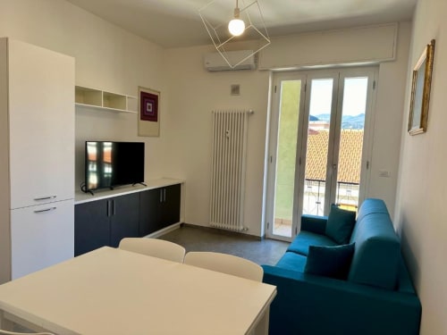 Soggiorno moderno con divano blu, tavolo da pranzo, angolo cottura e balcone con vista su Finale Ligure