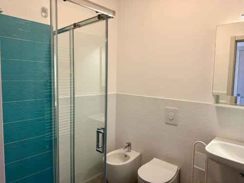 Bagno moderno nell'appartamento Grecale a Finale Ligure, con piastrelle turchesi, box doccia in vetro, wc e bidet