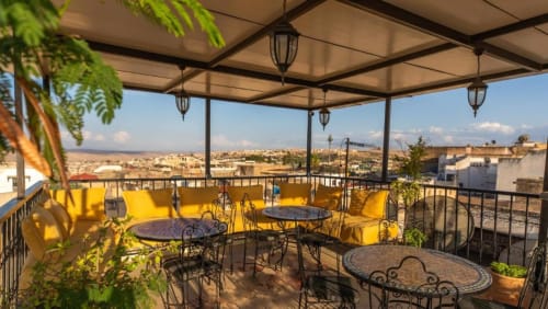 Terrasse sur le toit du Riad Dar Tahri à Fès avec sièges aux coussins jaunes, lanternes suspendues et vues panoramiques sur la ville