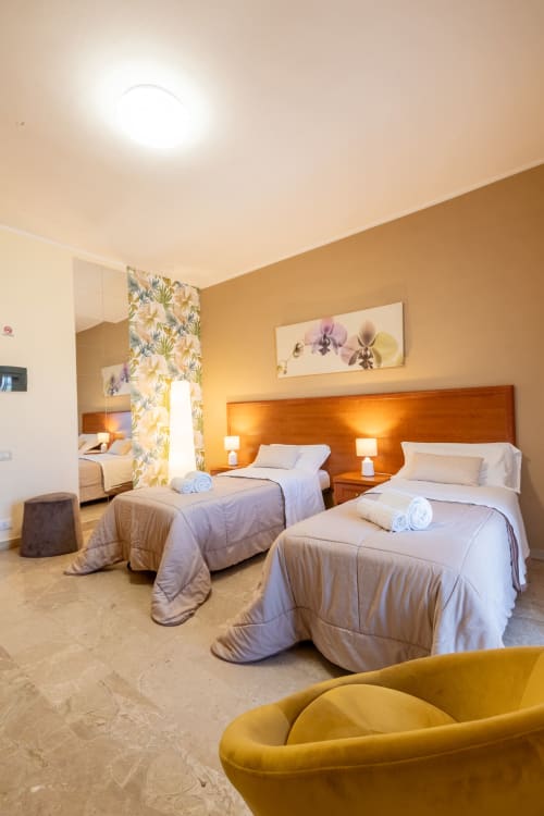 Camera luminosa di La Zagara Rooms a Milazzo con due letti, testata arancione, poltrona gialla e servizi moderni