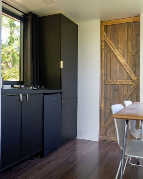 Cuisine moderne noire avec porte grange en bois et coin repas aux Cabanes de Julie, France
