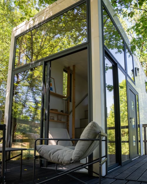Cabane moderne en verre aux Cabanes de Julie avec fauteuil gris sur la terrasse, vue sur la canopée forestière, Lissac et Mouret