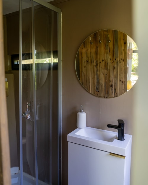Salle de bain moderne aux Cabanes de Julie avec lavabo blanc, robinetterie noire, miroir en bois et douche vitrée