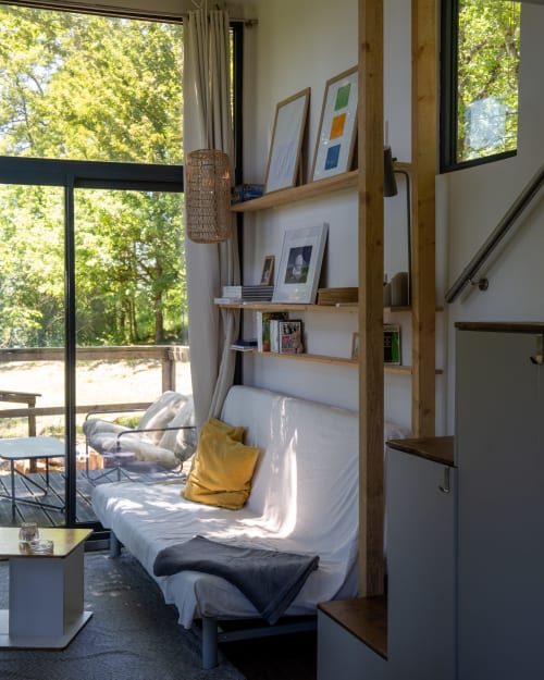 Coin chambre douillet aux cabanes de Julie avec lit, étagères en bois, art encadré et vue sur la forêt