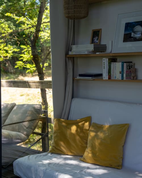 Chambre douillette aux Cabanes de Julie avec coussins jaunes, étagères en bois et vue forestière par la fenêtre