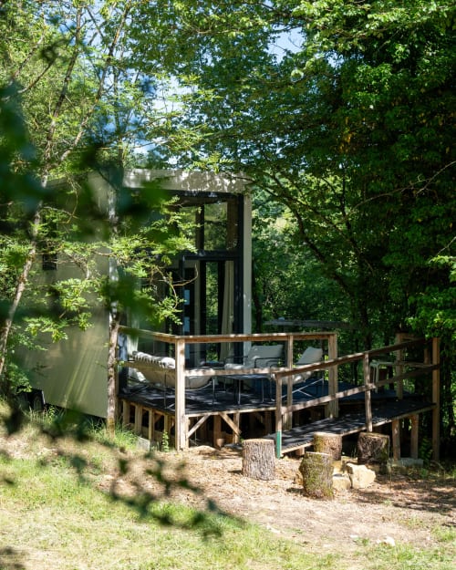 Cabane perchée aux Cabanes de Julie avec terrasse en bois, garde-corps noirs et forêt luxuriante à Lissac-et-Mouret
