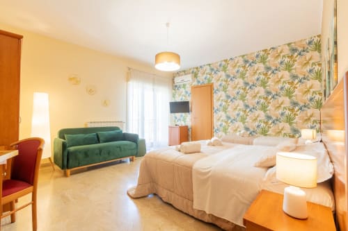 Ampia camera quadrupla presso La Zagara Rooms, Milazzo con letti gemelli, divano verde, carta da parati floreale e accesso al balcone