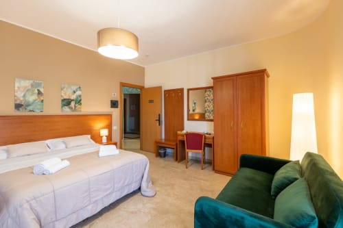 Ampia camera quadrupla a La Zagara a Milazzo con letto queen, divano verde, arredi in legno e vista sulla città