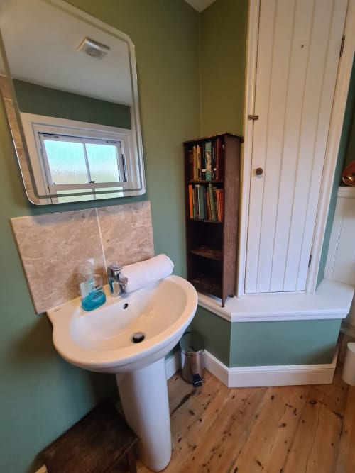 Bathroom at 2 Doves Holiday Property, Exeter with pedestal sink, mirror, tiled backsplash, wooden storage unit