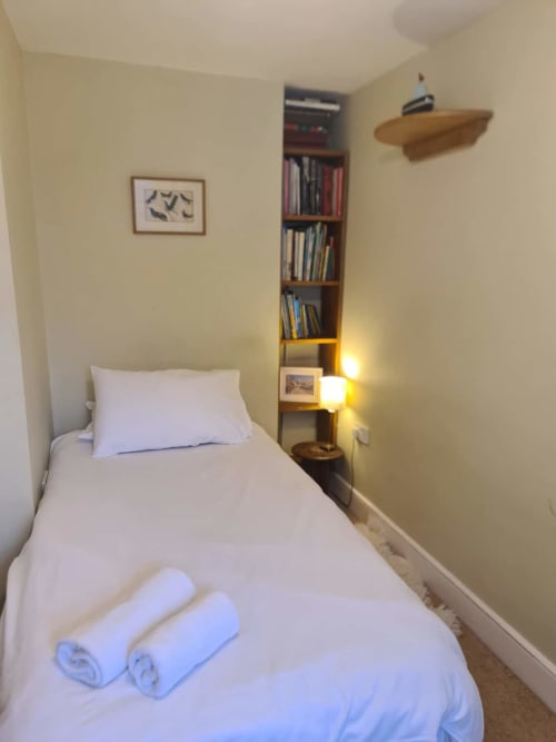 Compact single bedroom at 2 Doves Holiday Property, Exeter with white bedding, rolled towels, wooden shelf unit and framed