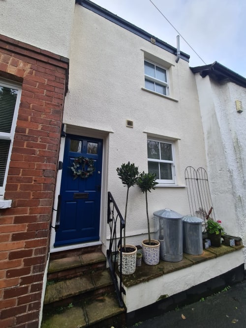 Charming cottage entrance at 2 Doves Holiday Property in Exeter with blue door, cream walls, and potted plants