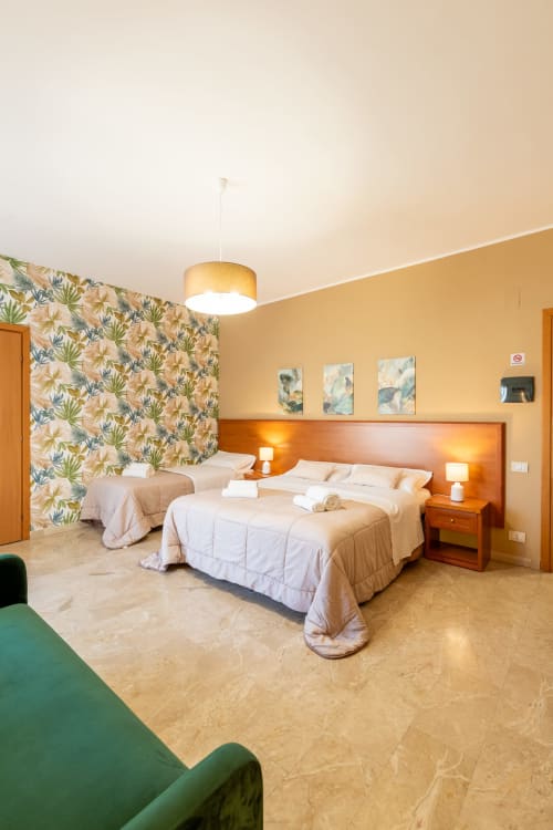 Spaziosa camera quadrupla a La Zagara Rooms di Milazzo con due letti, carta da parati floreale, testata in legno e vista sulla città