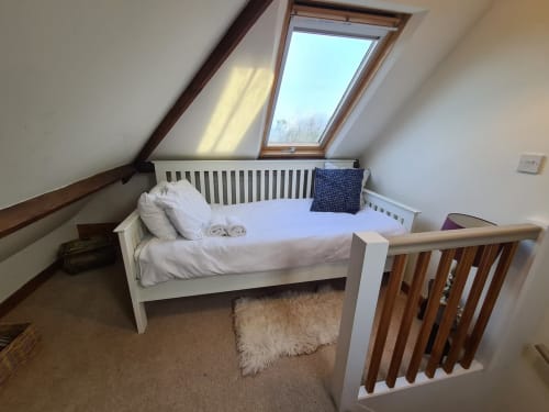 Attic bedroom with white single bed, skylight window, wooden beams, and fluffy white rug at 2 Doves Holiday Property, Exeter