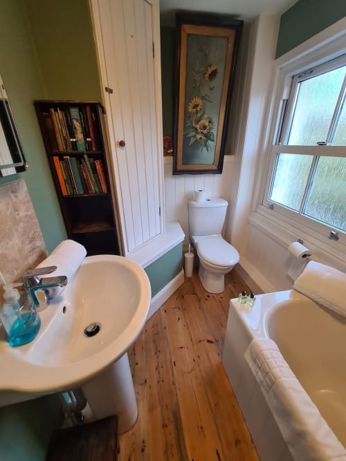 2 Doves Holiday Property bathroom in Exeter with white suite, wooden floor, sunflower artwork, and window