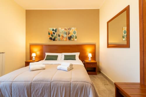 Camera accogliente di La Zagara Rooms a Milazzo con testata in legno, biancheria bianca e illuminazione calda