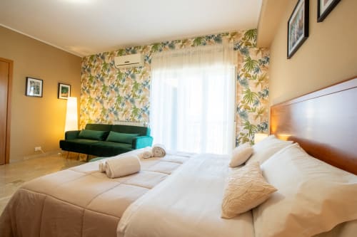 Camera luminosa a La Zagara Rooms di Milazzo con letto bianco, divano verde e carta da parati tropicale