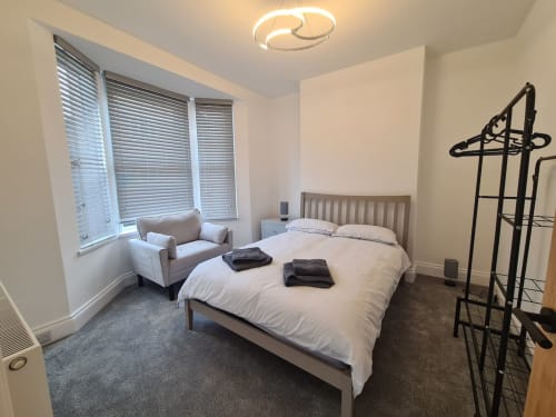 Modern bedroom at 2 Doves Holiday Property in Exeter with queen bed, armchair, and bay windows with blinds