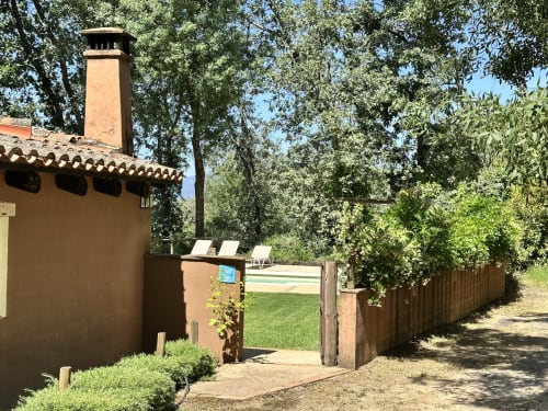 Rustic Spanish countryside estate entrance with clay walls, chimney, wooden gate, and surrounding olive trees at El Escondite