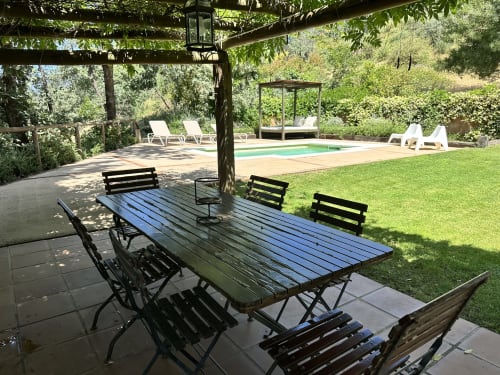 Outdoor dining area with black table and chairs under pergola, swimming pool and green garden at El Escondite De Pedro