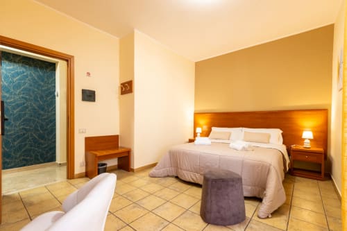 Camera luminosa a La Zagara Rooms Milazzo con letto matrimoniale, arredamento in legno e porta con vista sul mare